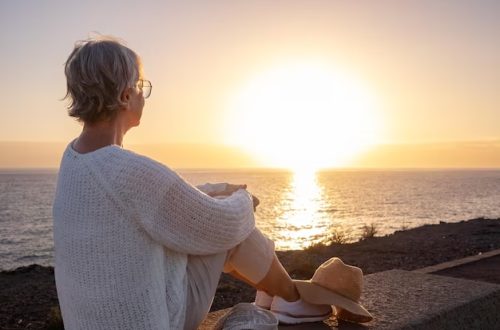 vista-traseira-da-mulher-senior-relaxada-e-romantica-ou-pensionista-sentada-admirando-o-mar-a-luz-do